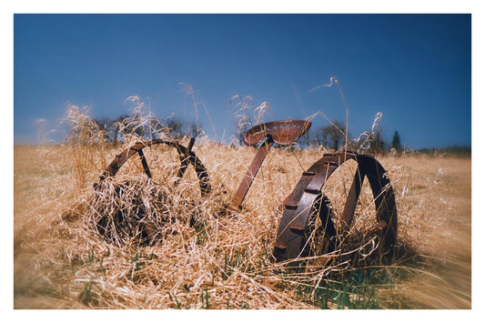 Retired Hay Mower, Gallery Edition print: a rusting horse-drawn hay mower in dry golden grass under a blue sky