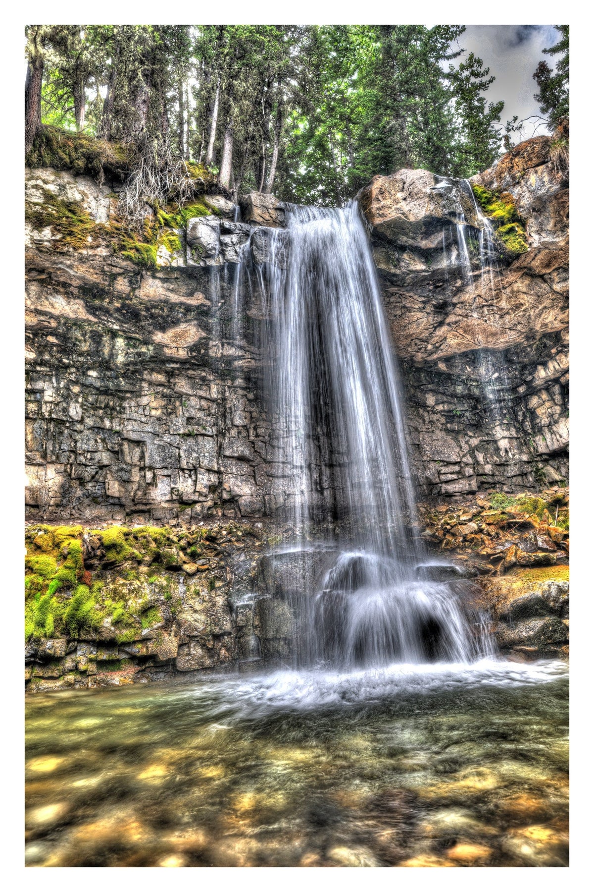 Marmot Falls in Kananaskis Country, Alberta, pouring over mossy stacked rock ledges into a clear forest pool — Gallery Edition print with a white border