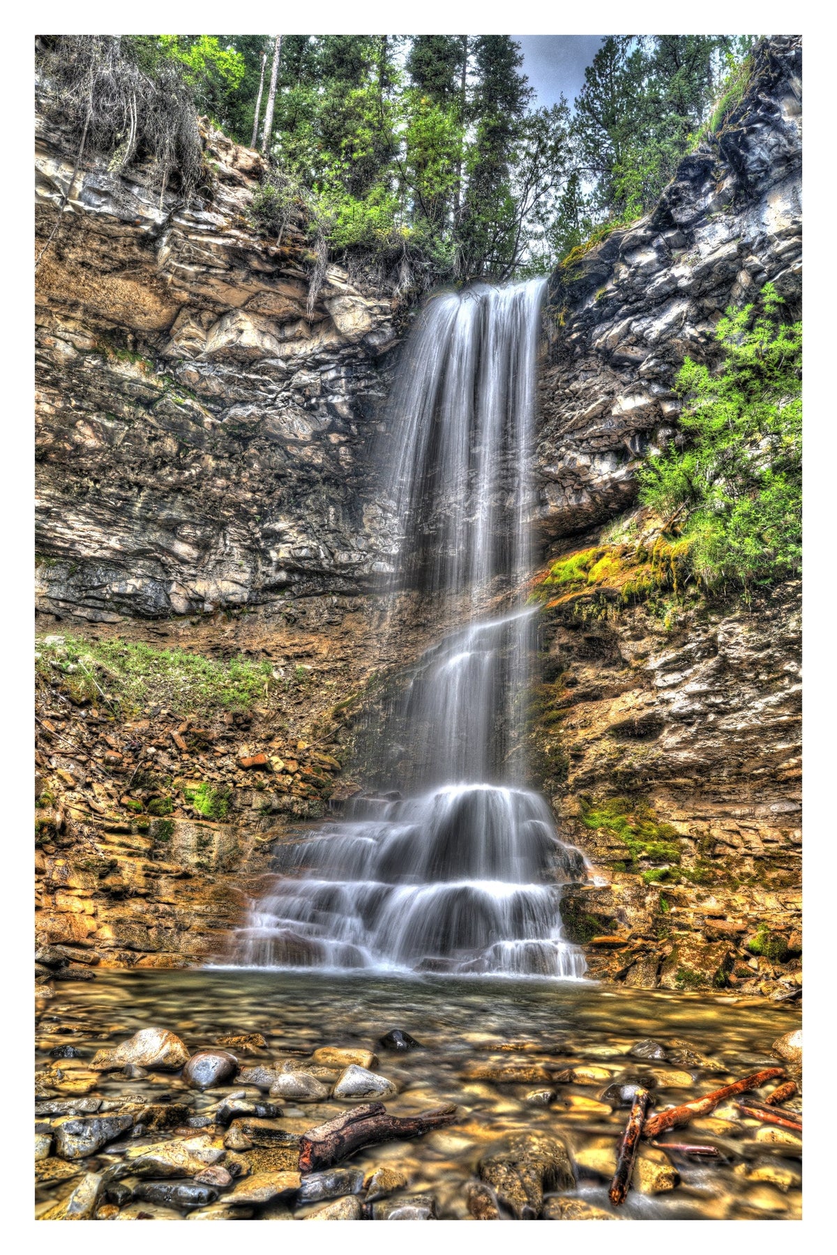 Troll Falls in Kananaskis Country, Alberta, cascading down a layered rock cliff into a pool of stream-worn stones — Gallery Edition print with a white border