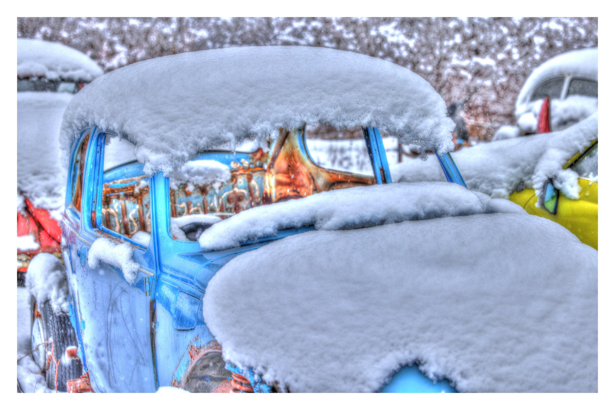 Sky-blue Volkswagen Beetle under a thick blanket of fresh snow among other old cars — Winter Bugs Gallery Edition print with a white border